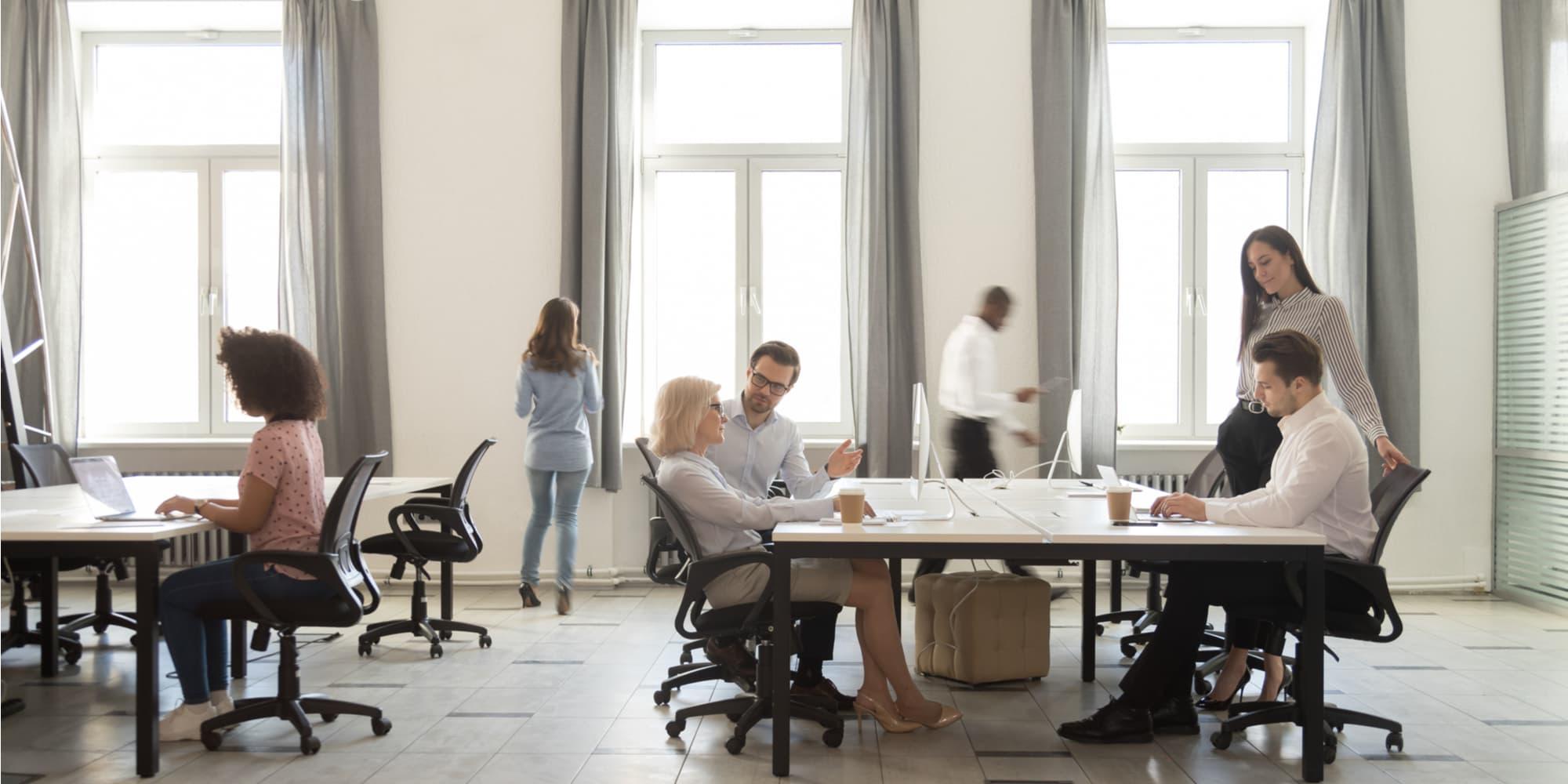 繁忙的公司部门成员，员工一起工作，坐在共享的桌子上，使用电脑，在现代的共同工作空间，室内日光透过窗户